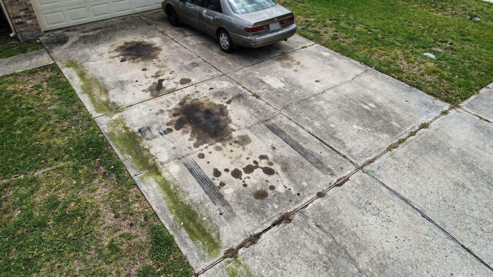 Concrete driveway with oil stains and algae streaks before B&R pressure washing service